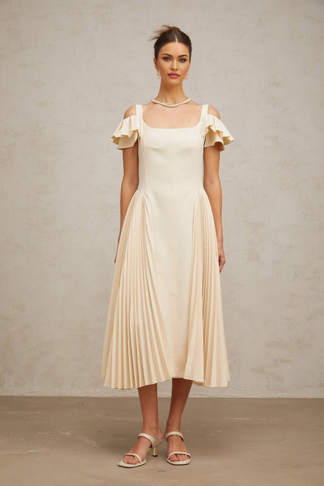 Woman wearing long beige pleated midi dress with flared skirt and neutral tones standing in relaxed pose