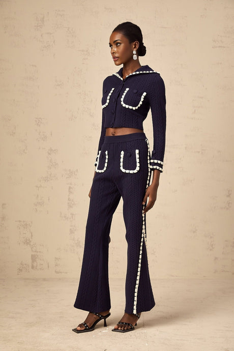 Woman wearing navy blue crochet knit cardigan and matching trousers set standing against plain background