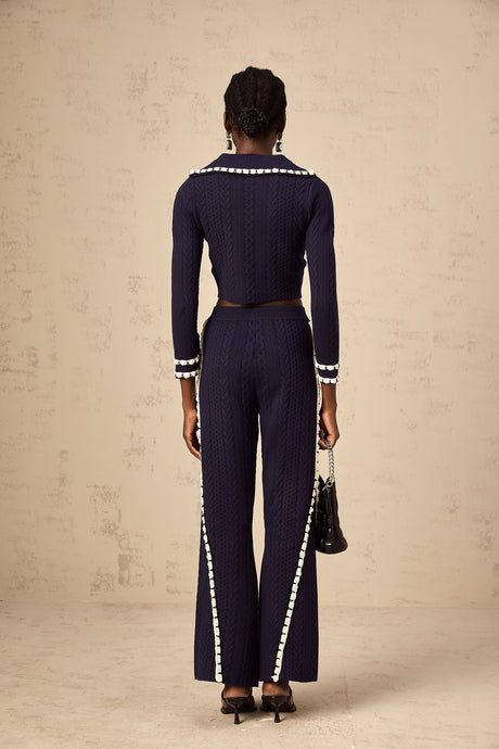 Woman wearing navy blue crochet knit cardigan and matching trousers standing against plain background
