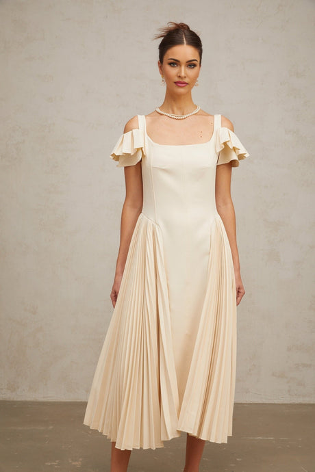 Woman wearing neutral colored pleated flared midi dress with long sleeves and V neckline