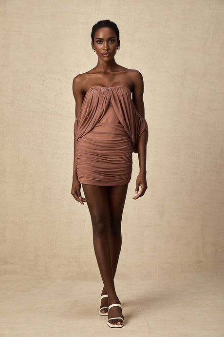Woman wearing offshoulder bodysuit and matching skirt set in light color standing with hands on hips
