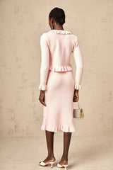Woman wearing pink argyle pattern knitted cardigan and matching skirt set against plain background