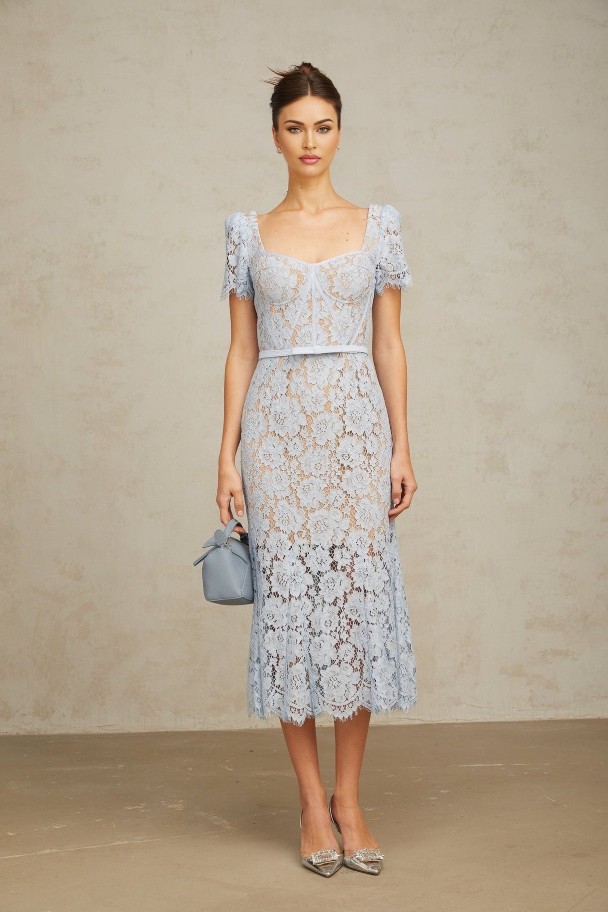 Woman wearing sleeveless blue midi dress with floral lace pattern and boned bodice