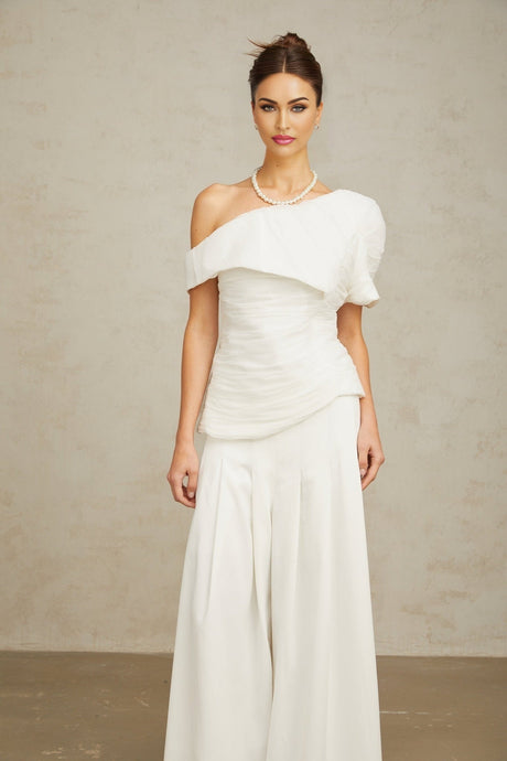 Woman wearing white creased fabric top and matching trousers standing against plain background