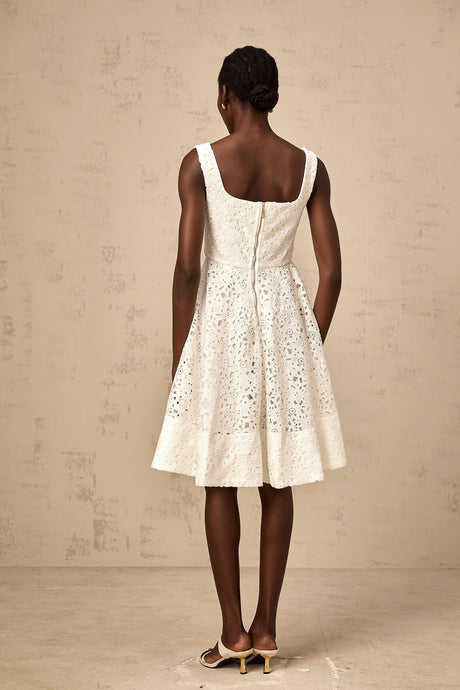 Woman wearing white floral lace midi dress with fitted bodice and flowing skirt standing against plain background