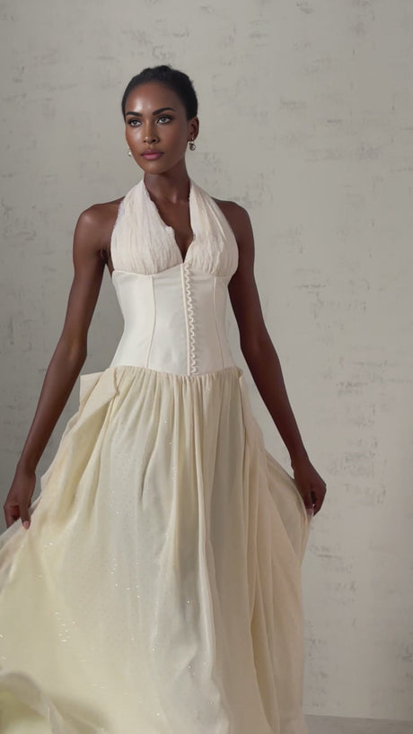 Woman wearing white halterneck tulle midi dress with flared skirt and fitted bodice standing in neutral background