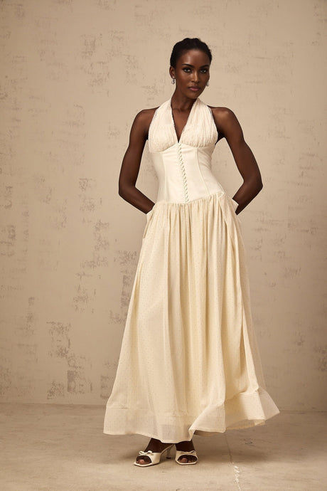 Woman wearing white halterneck tulle midi dress with floral embroidery standing in front of plain background