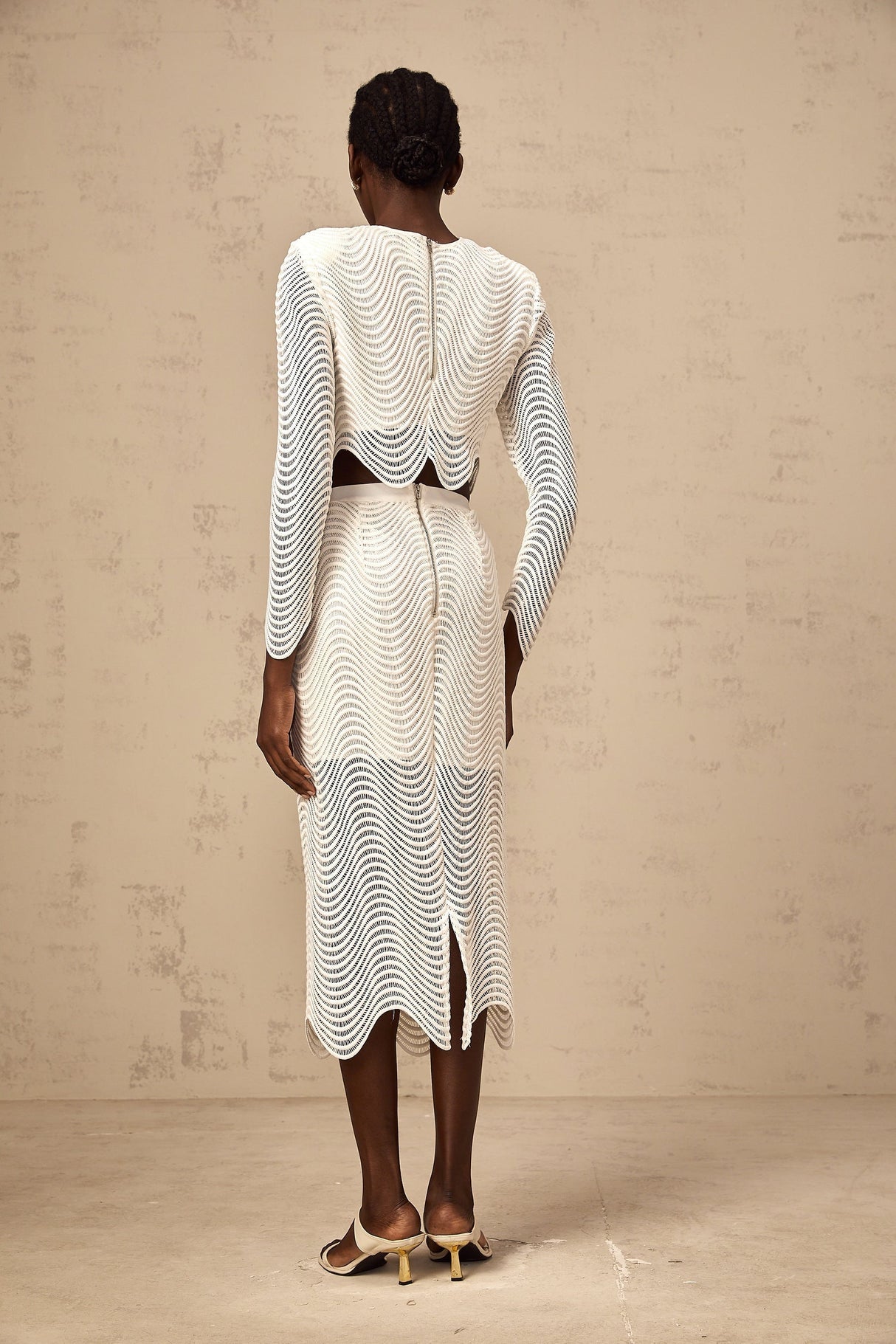 Woman wearing white matching set with wavy woven texture top and skirt standing against plain background