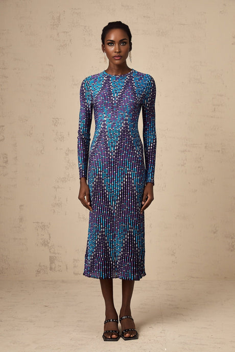 Young woman wearing a blue and white zigzag pattern knitted midi dress with long sleeves standing against a plain background