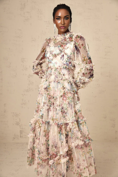 Young woman wearing a floral patterned midi dress with ruffled details and tulle overlay standing in front of a plain background