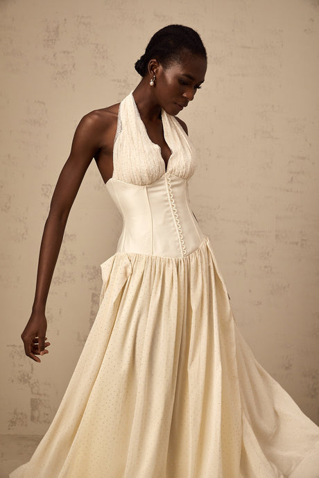 Young woman wearing a light pink halterneck tulle midi dress with a fitted bodice and flowy skirt standing in a neutral background