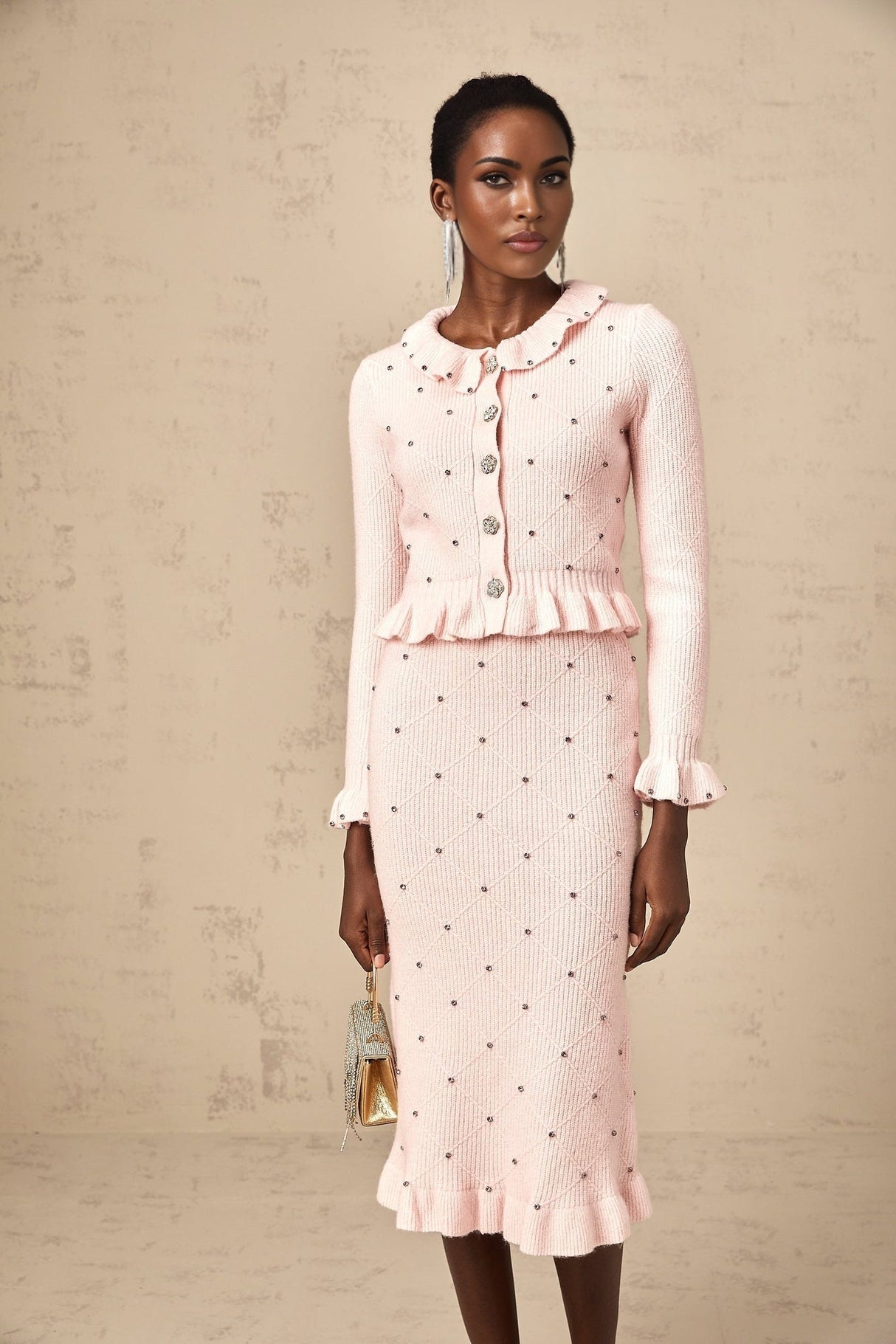 Young woman wearing a pink argyle patterned knit cardigan and matching skirt set against a plain background