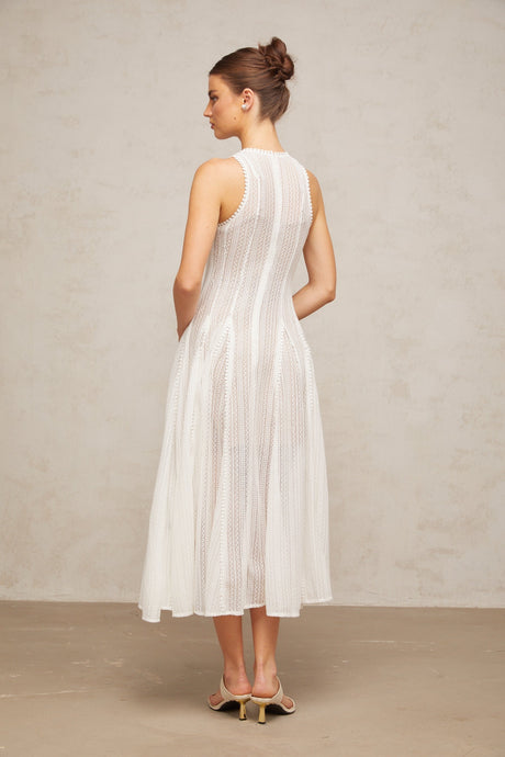 Young woman wearing a white midi dress with pointelle detailing and puff sleeves standing in a neutral background