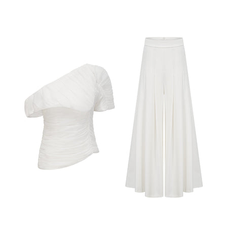 Young woman wearing white Adele matching set with creased top and trousers standing against plain background